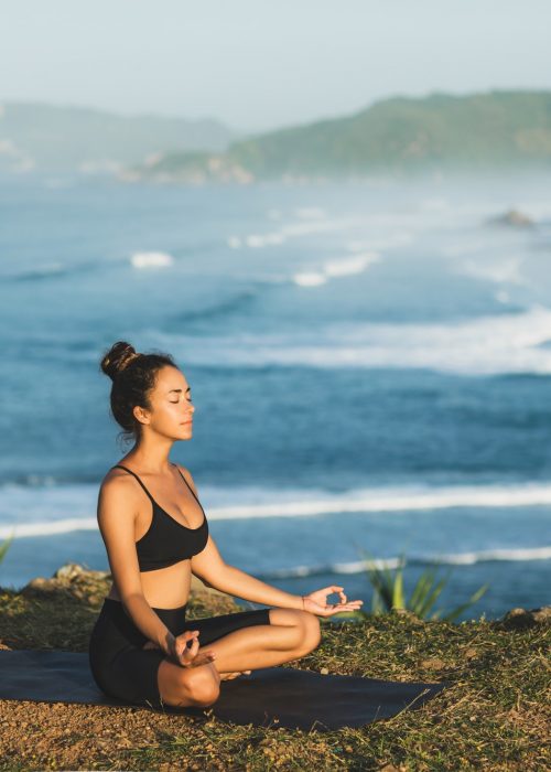 Woman practicing yoga and sitting in lotus pose outdoor with amazing ocean view. Nature background.